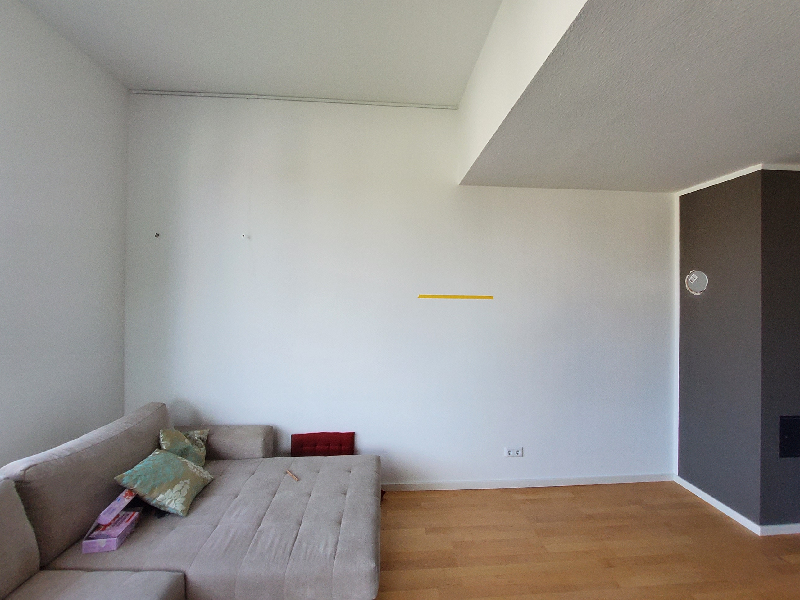A living room with minimalist design, featuring a beige sectional sofa, plain white walls, light wood flooring, and a dark accent wall, calm atmosphere.