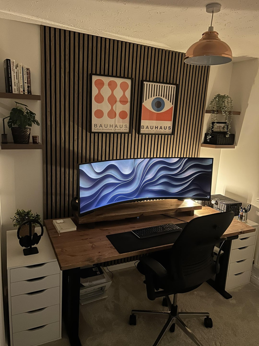 Compact home office with wood slat wall, ultrawide monitor, and Bauhaus artwork