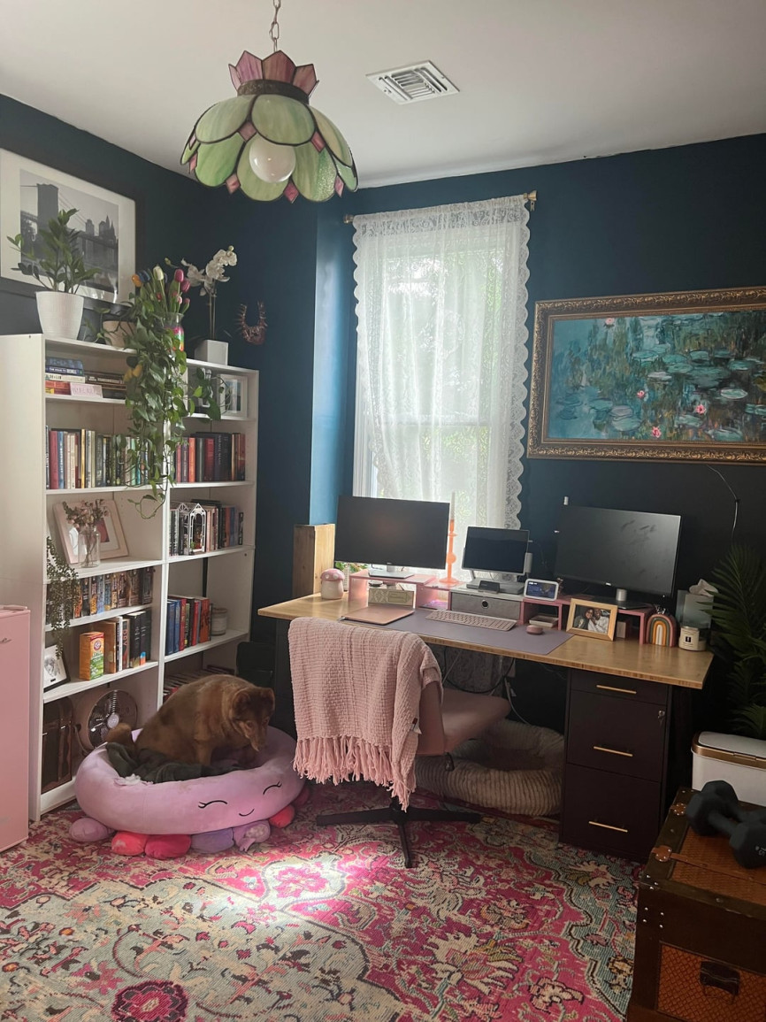 Dark home office with desk setup, bookshelf, and moody blue walls