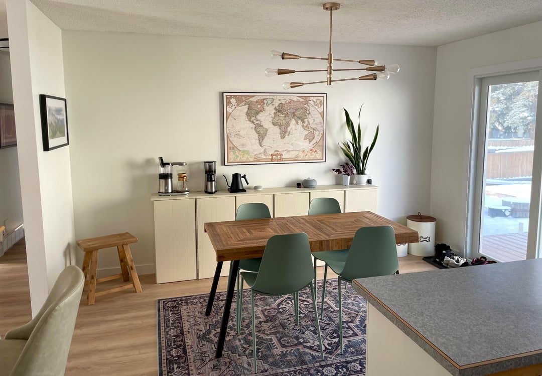 Dining room with wood table, green dining chairs, patterned rug, and modern brass ceiling light
