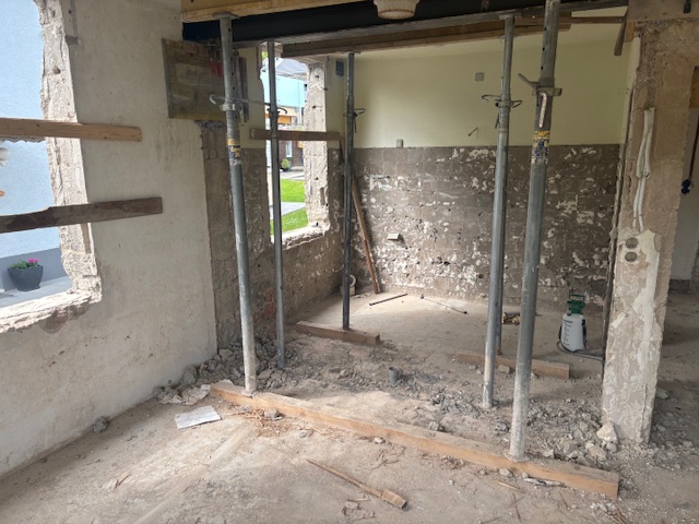 Under construction interior space featuring exposed brick walls, concrete floor, metal support poles, and partially demolished window openings.