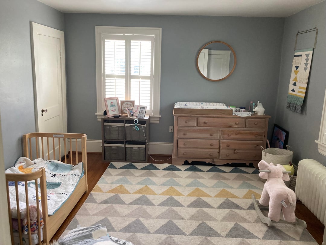 Kids nursery with gray blue walls, geometric rug, wooden toddler bed, dresser, and rocking unicorn toy