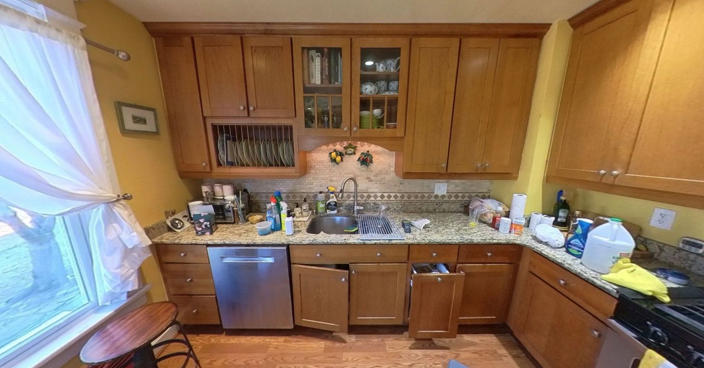 Lshaped kitchen with traditional wooden cabinets, granite countertops, stainless steel appliances, yellow walls, cluttered surfaces, and natural light from a window.