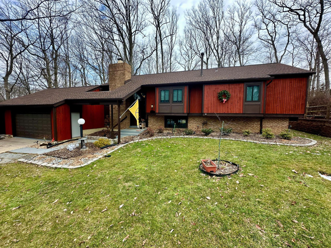 Dark cedar mid-century ranch house exterior with large front lawn and wooded surroundings