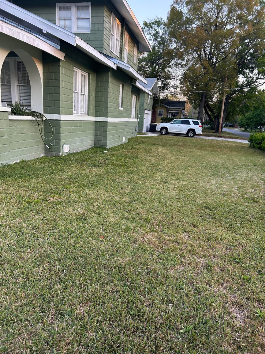 Plain grass lawn beside green Craftsman-style house with minimal landscaping