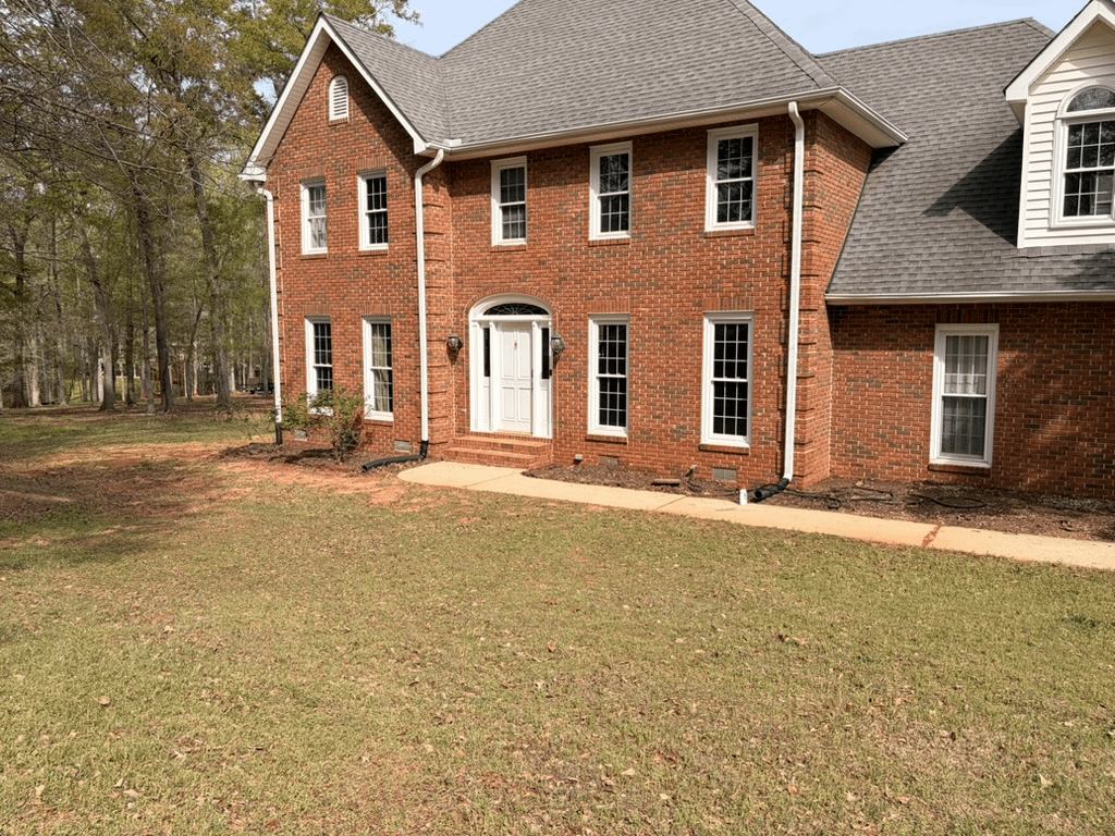 Large red brick Colonial home with sparse front yard landscaping and open lawn
