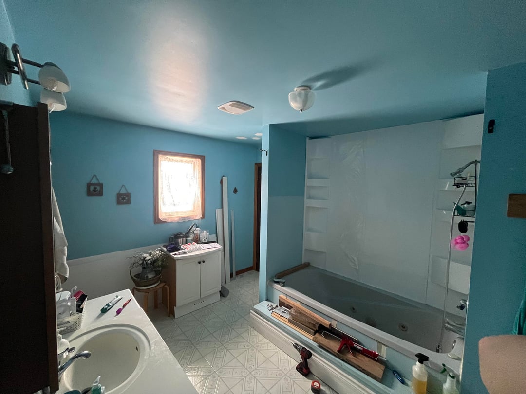 Bathroom with bright blue walls, built in bathtub, patterned floor tiles, and white vanity cabinet