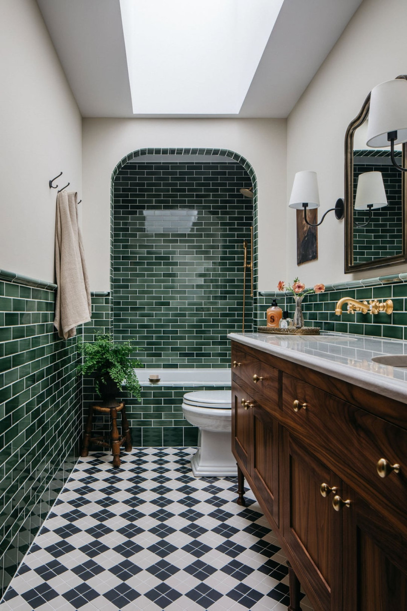 Bathroom with dark green subway tiles, walnut vanity, brass fixtures, and arched shower alcove