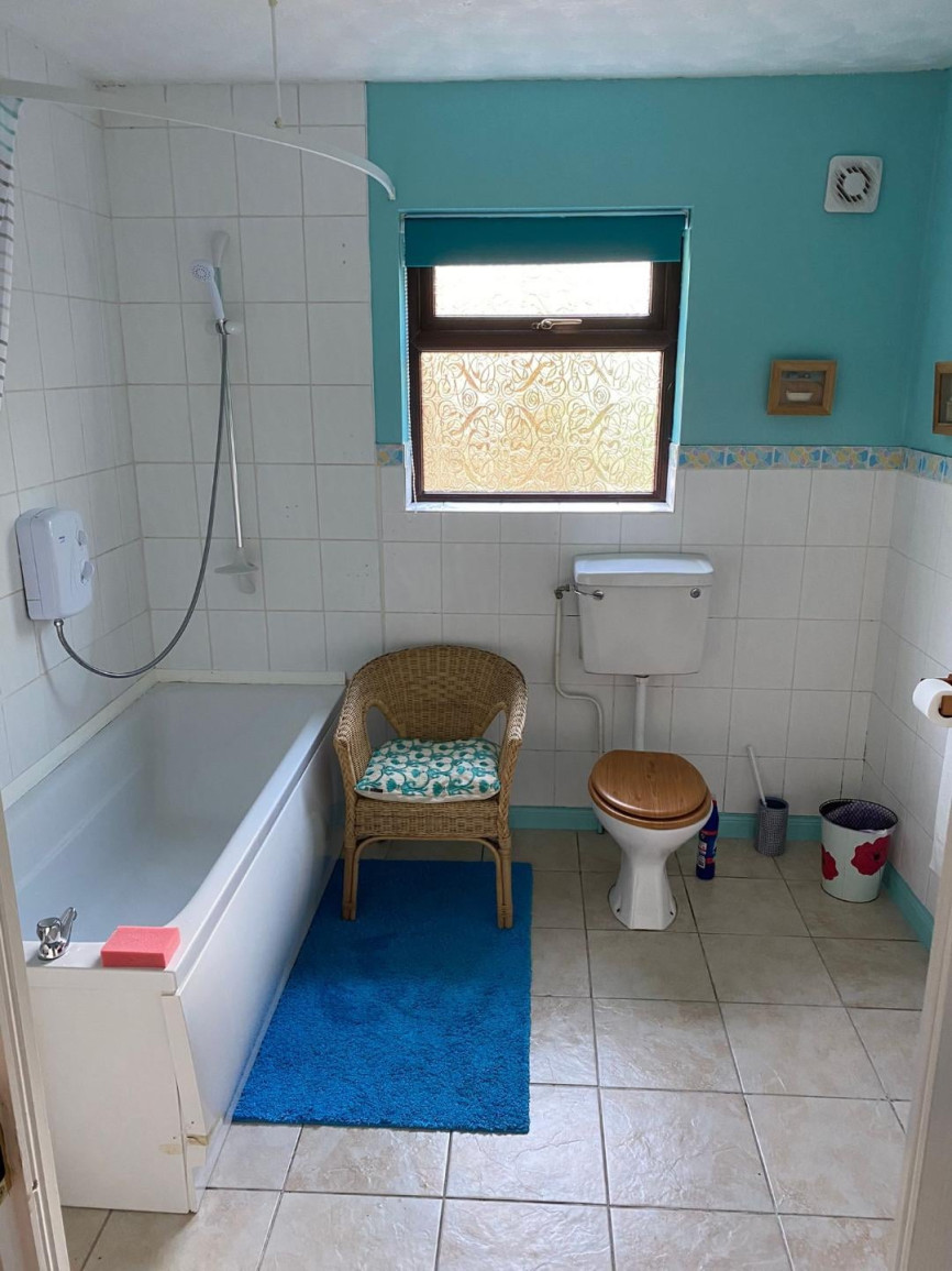 Outdated bathroom with turquoise walls, bathtub shower combo, wicker chair, and patterned window covering