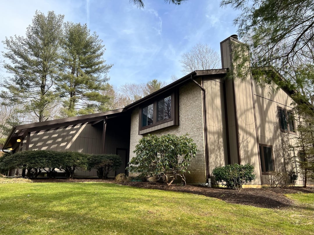 Suburban yard with open lawn, mature trees, foundation shrubs, and minimal garden planting