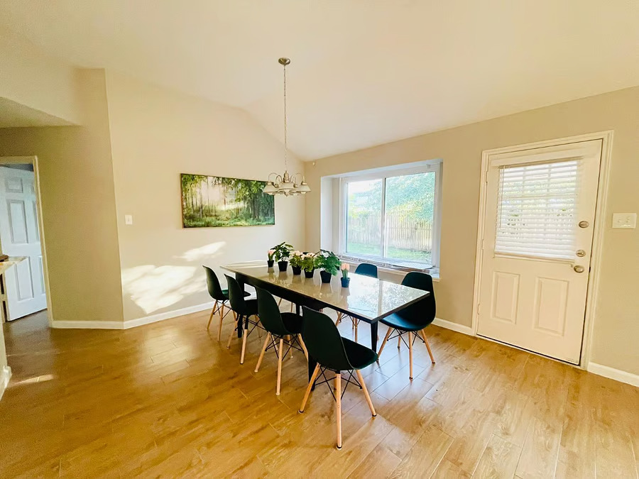Dining room with black chairs, wood table, beige walls, window blinds, and light wood flooring