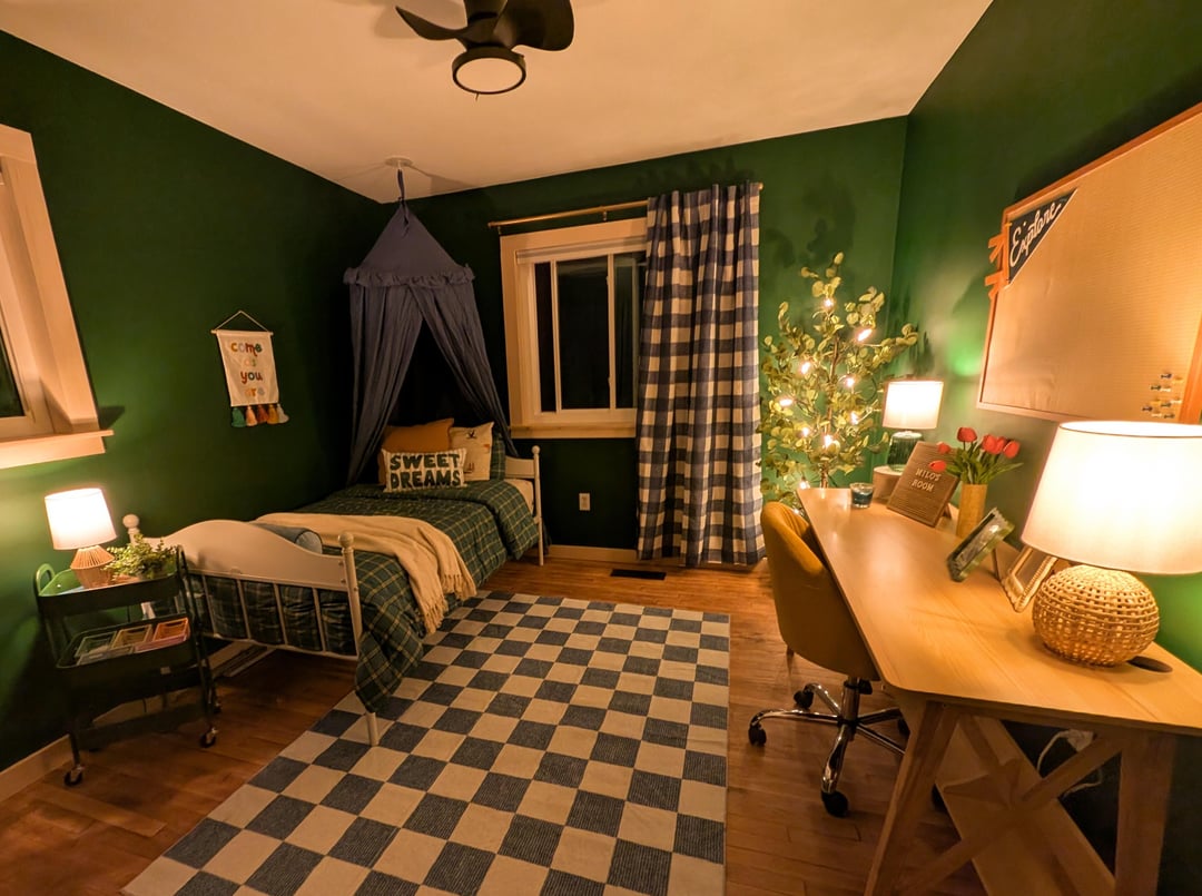 Kids bedroom with dark green walls, checkered rug, canopy bed, plaid curtains, and wooden desk setup