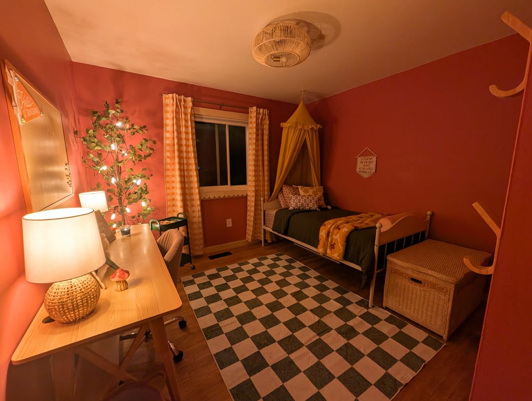 Kids bedroom with dark red walls, checkered rug, corner bed, and small desk beside a narrow window.