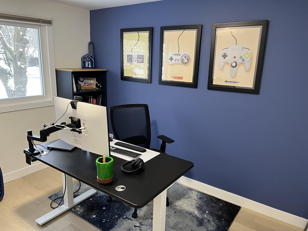 Home office with blue accent wall, standing desk, and gaming artwork