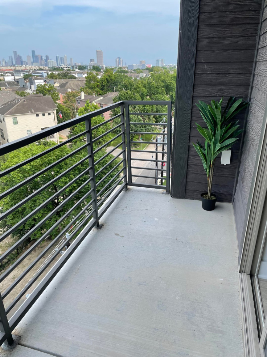 Narrow high-rise apartment balcony with concrete floor, black railing, and skyline view