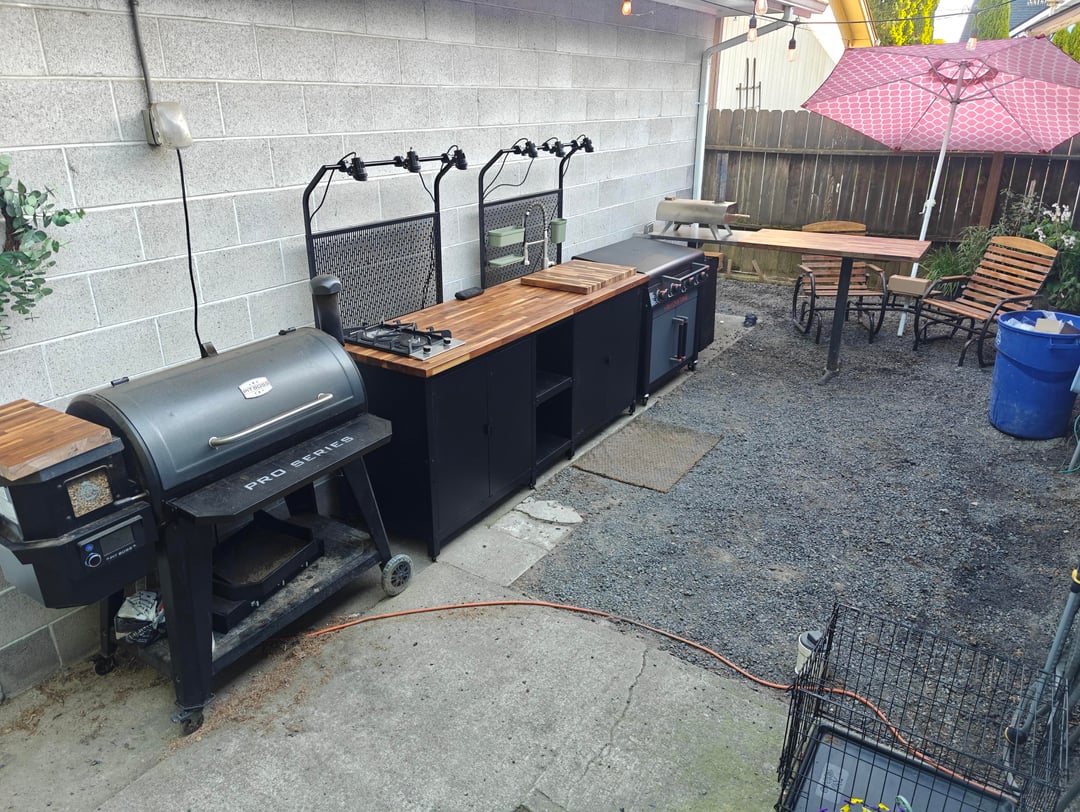 Basic outdoor kitchen setup with grills, prep counters, and gravel backyard patio