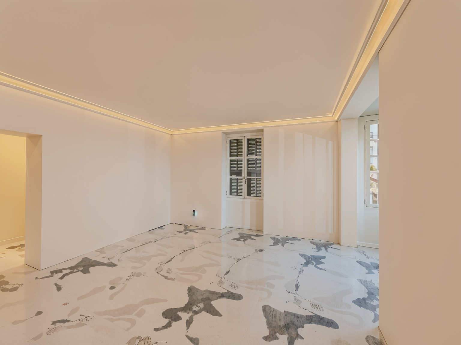 Empty modern kitchen space with white walls, large abstract gray and white marble floor tiles, recessed ceiling lighting, and natural light from shuttered windows.