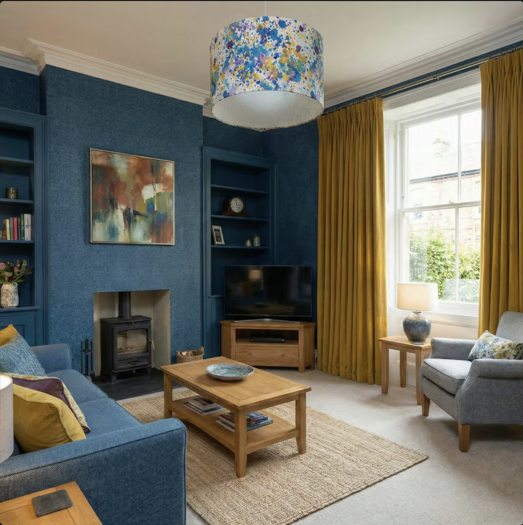 Traditional living room with deep blue walls, mustard yellow curtains, wooden furniture, a wood-burning stove, and a colorful abstract lampshade.