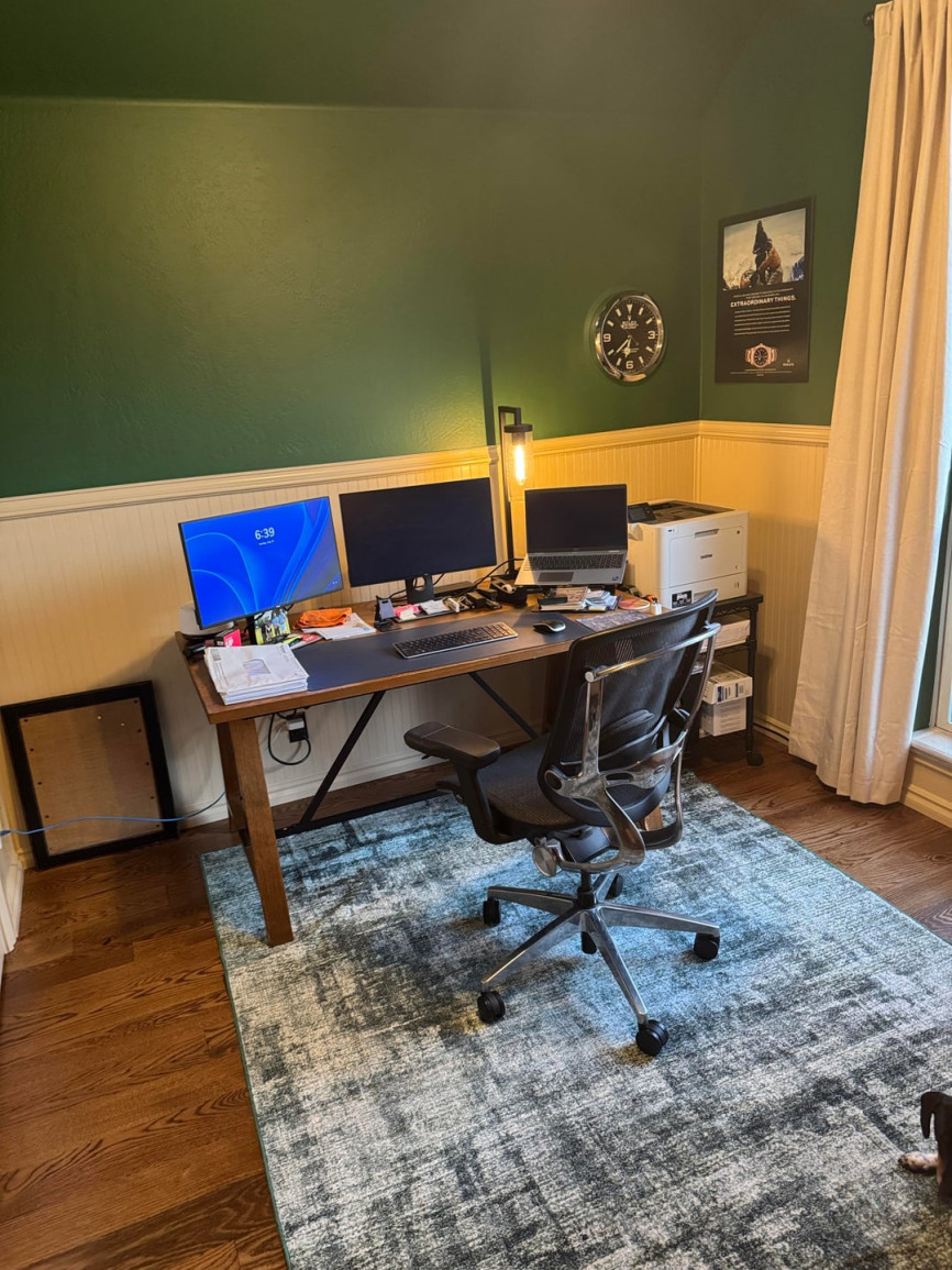 Small home office with green walls, desk setup, and office chair.