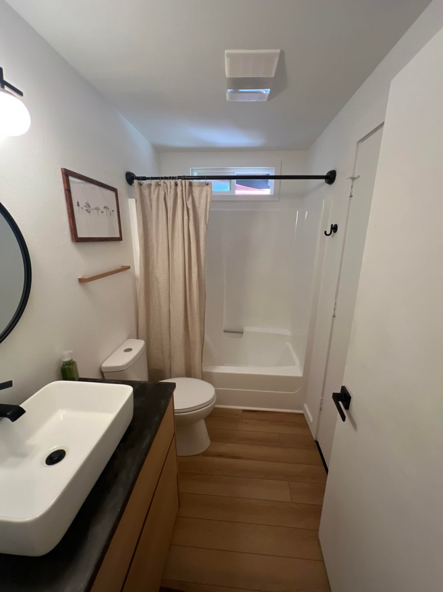 Small bathroom with dark countertop vanity, beige shower curtain, white shower insert, and wood flooring